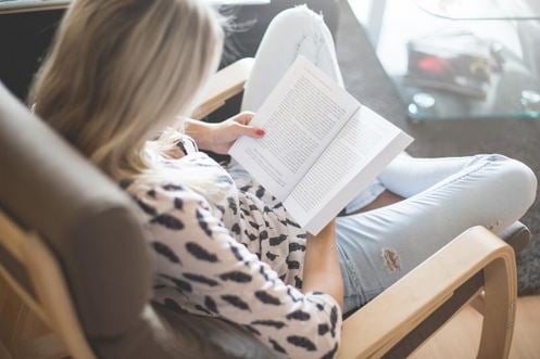 Vaaleahiuksinen nainen lukee kirjaa nojatuolissa
